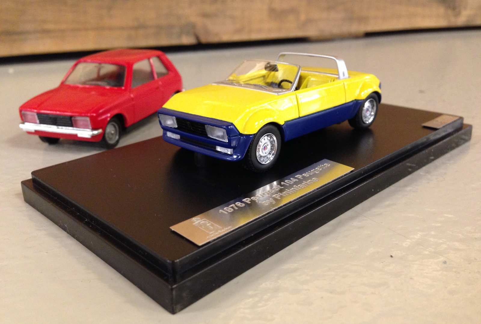 Een model van een geel-blauwe Peugeot Peugette op standaard.