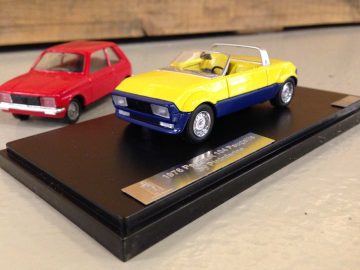 Een model van een geel-blauwe Peugeot Peugette op standaard.