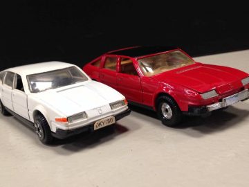 Twee Dinky Toys autootjes naast elkaar op een witte ondergrond.