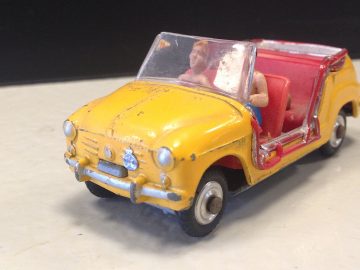 Een gele speelgoedauto met een man op de bestuurdersstoel, die doet denken aan AutoRAI in Miniatuur.