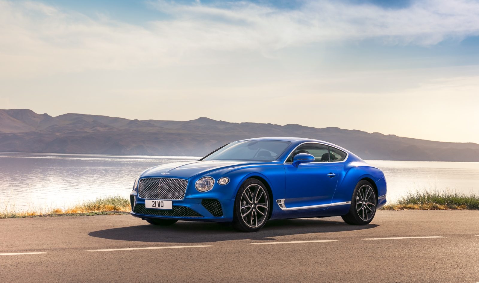 Een blauwe Bentley Continental GT geparkeerd op een weg naast een watermassa.