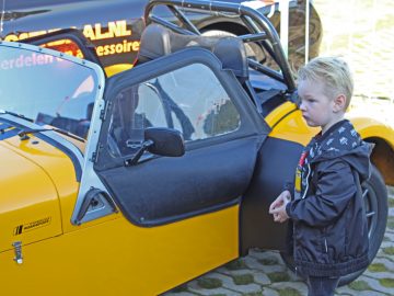 Een jonge jongen staat naast een gele sportwagen op de Borderrun Fly-in Car Show 2017.