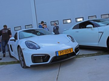 Een witte Porsche Cayman geparkeerd voor een gebouw tijdens de Borderrun Fly-in Car Show 2017.