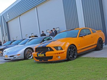 Een groep oranje en zwarte sportwagens geparkeerd voor een gebouw op de Borderrun Fly-in Car Show 2017.