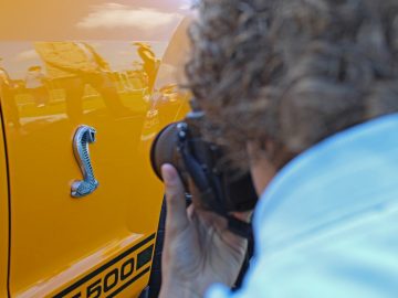 Een vrouw die een foto maakt van een gele vrachtwagen tijdens de Borderrun Fly-in Car Show 2017.