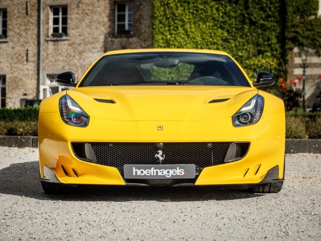 Een gele Ferrari F12tdf sportwagen te koop, geparkeerd voor een huis in Limburg.