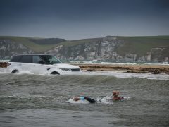 Een man zwemt in de oceaan vlakbij een witte Range Rover Sport P400e.