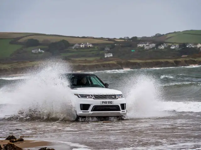 Een witte Range Rover Sport P400e die over het strand rijdt.