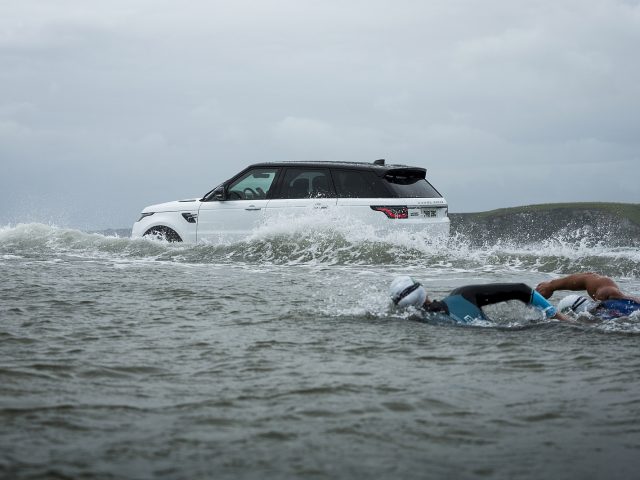 Een man zwemt in de oceaan met een Range Rover Sport P400e.