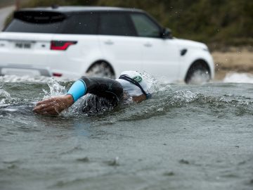 Een man zwemt in het water vlakbij een Range Rover Sport P400e.