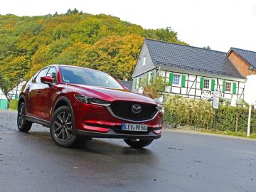 De rode Mazda CX-5 Skyactiv-G 194 staat voor een huis geparkeerd.