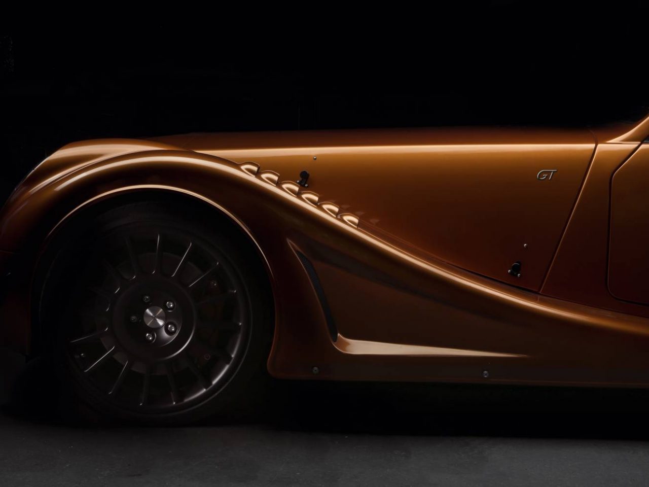 Een oranje Morgan Aero 8 wordt getoond in een donkere kamer.