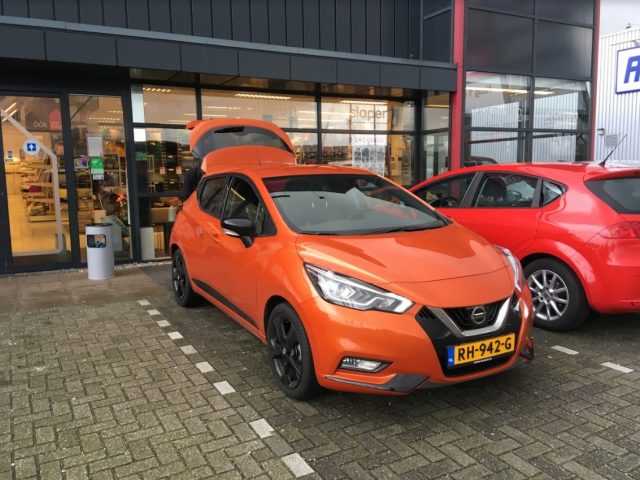 Twee oranje Nissan Micra's geparkeerd voor een winkel.