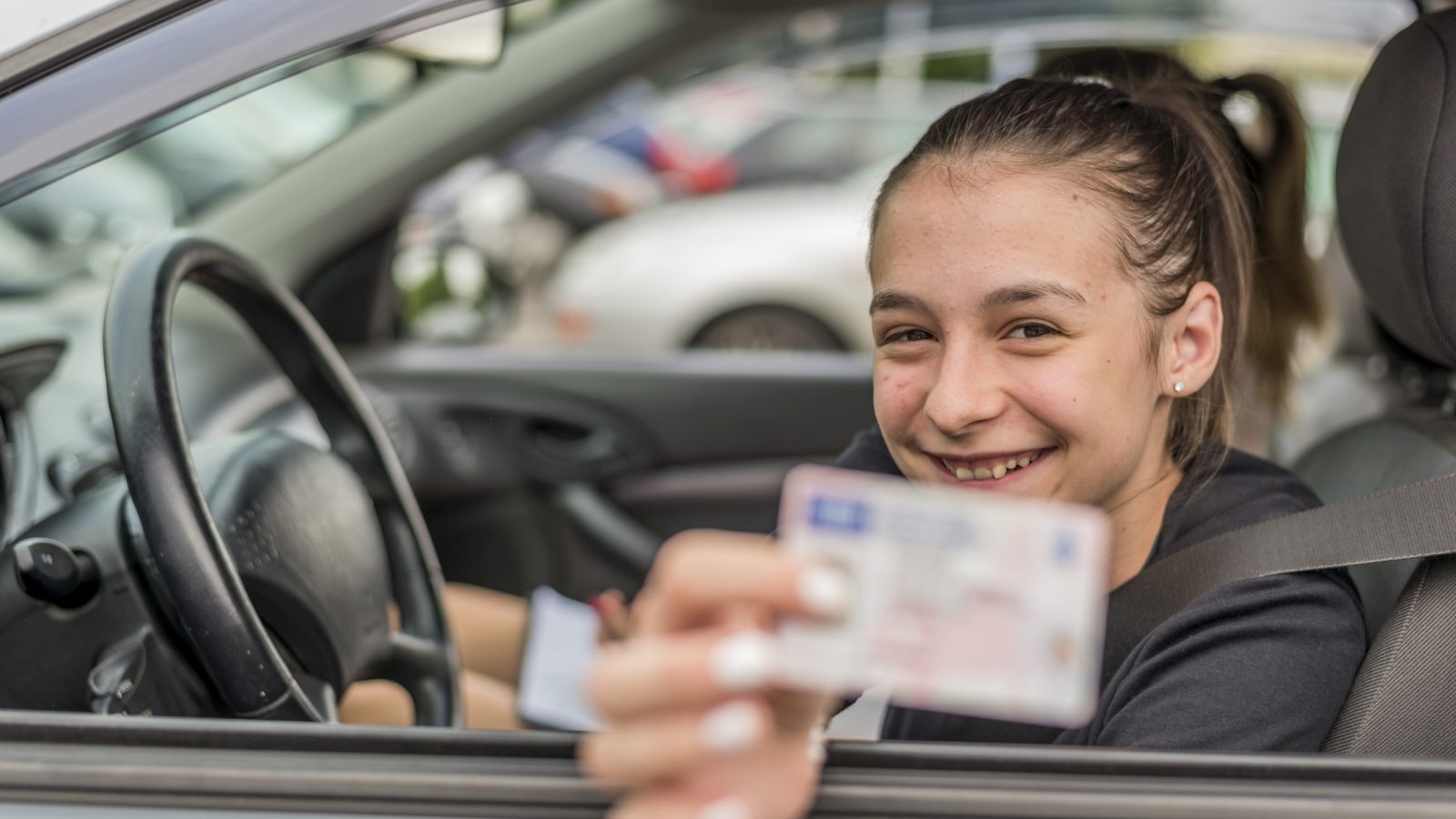 Een meisje in een auto met een rijbewijs voor 'Begeleid rijden voor 17-jarigen.