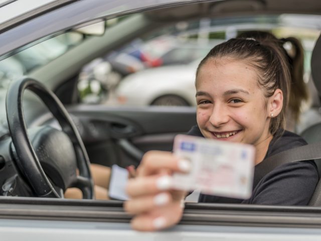 Een meisje in een auto met een rijbewijs voor 'Begeleid rijden voor 17-jarigen.