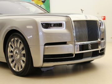 In een kamer staat een zilverkleurige nieuwe Rolls-Royce Phantom geparkeerd.