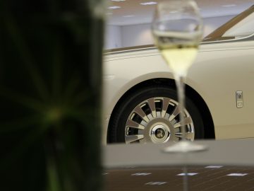 Een glas champagne op een tafel naast een nieuwe Rolls-Royce Phantom.