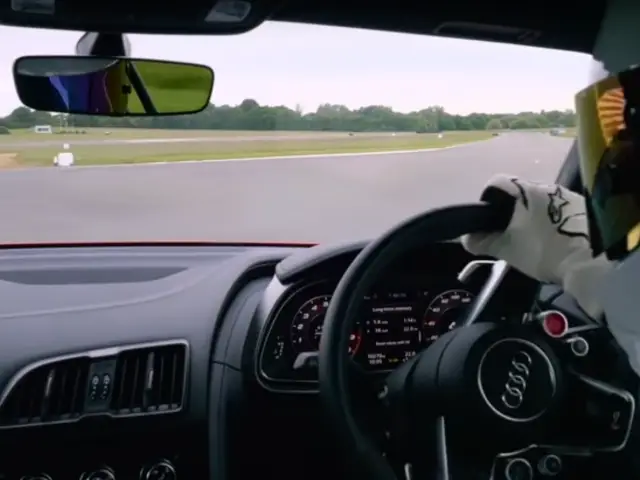 De Stig, met helm op, rijdt in een Audi R8 op een circuit.