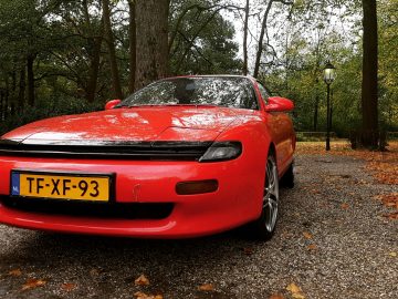 Een rode auto geparkeerd in een bebost gebied.