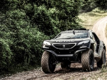 Een zwarte Dakar-monstertruck rijdt over een onverharde weg.