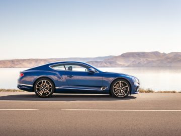 De blauwe Bentley Continental GT, met houtverwerkingsdetails, staat langs de kant van de weg geparkeerd.