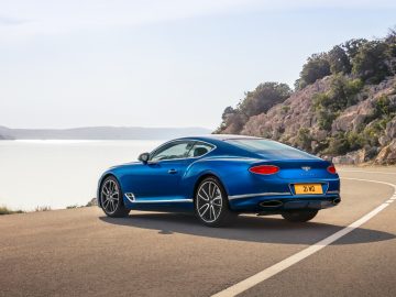 De blauwe Bentley Continental GT rijdt over een weg van drie meter langs een meer.