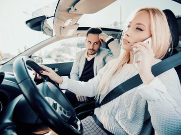 Een man en bijrijder in een auto praten aan de telefoon.