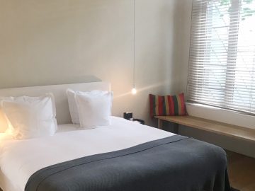 Een bed in een kamer met houten vloer en een raam met uitzicht op een culinair avontuur.