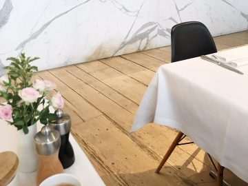 Een witte tafel met bloemen, een kop koffie en een brochure voor een culinair avontuur.