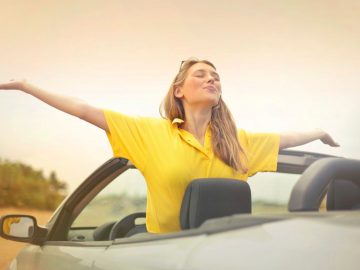 Een jonge vrouw in een tweedehands cabrio met haar armen uitgestrekt.
