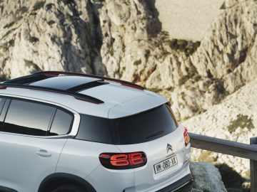 Het achteraanzicht van een witte Citroën C5 Aircross SUV uit 2019, geparkeerd aan de zijkant van een berg.