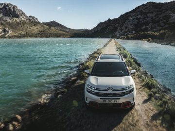 Een witte Citroën C5 Aircross SUV rijdt over een weg naast een watermassa.