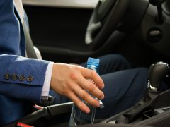 Een man die een flesje water vasthoudt in een auto.