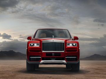 Een rode Rolls-Royce Cullinan staat geparkeerd in de woestijn.