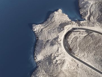 Een luchtfoto van een kronkelende weg vlakbij de oceaan, met een Rolls-Royce Cullinan.