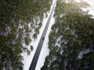 Luchtfoto van een besneeuwde weg in een bos, met een Rolls-Royce Cullinan zichtbaar.