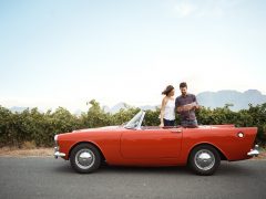 Een man en een vrouw zitten in een rode cabriolet, terwijl de man navigeert.