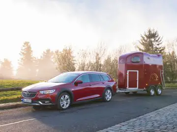 Een rode auto van Opel Insignia met een aanhangwagen.