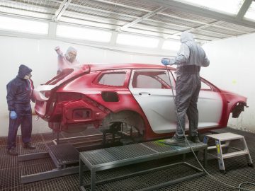 Twee mensen werken in een garage aan een rode Opel Insignia.