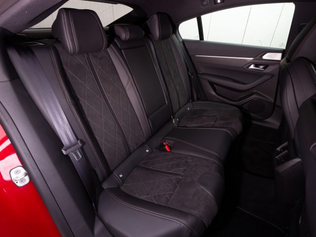 De achterbank van een rode Peugeot 508 met zwart lederen stoelen.