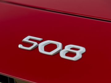 Een close-up van het Peugeot 508-embleem op een rode sportwagen.