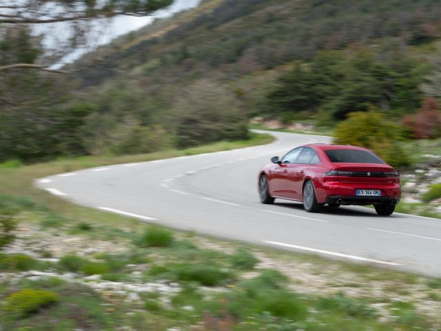 Een rode Peugeot 508 rijdt over een bochtige weg.