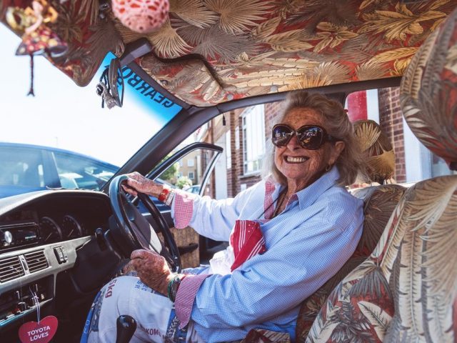 Een oudere vrouw zit op de bestuurdersstoel van een Corolla.