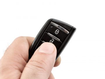 Een persoon die een keyless entry-afstandsbediening vasthoudt op een witte achtergrond.