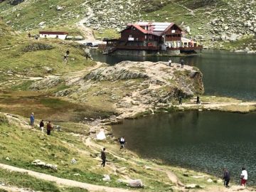 Een groep mensen staat aan de kant van de Transfagarasan, naast een meer.