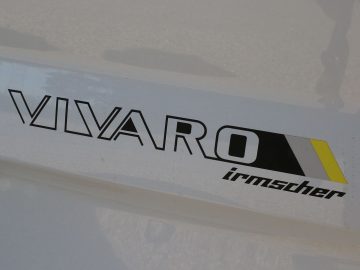 Een witte Opel Vivaro met een geel-zwart logo erop.