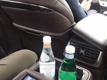 Een man zit in een auto met een fles water en luistert naar JRE.