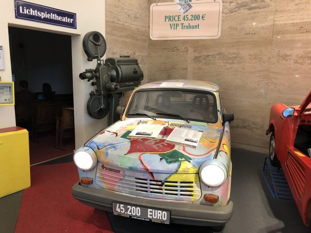 In een museum staat een kleurrijke Trabant-auto tentoongesteld.