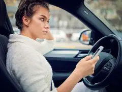 Een vrouw die op de bestuurdersstoel van een auto zit en naar haar mobiele telefoon kijkt die is verbonden met Android Auto.