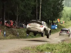 Een rallyauto die een stunt doet en over een onverharde weg vliegt.